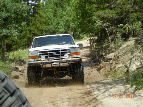1996 Ford Bronco - White 1996 Ford Bronco navigates a muddy trail surrounded by trees.