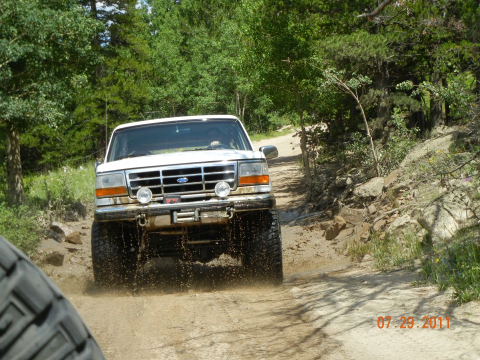 1996 Ford Bronco driving through mud on a dirt road, front view