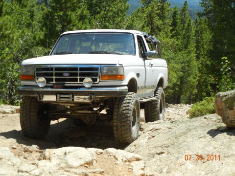 1996 Ford Bronco - A white 1996 Ford Bronco navigates a challenging rocky path surrounded by trees.