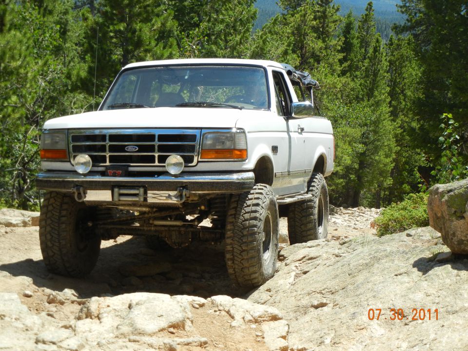 White 1996 Ford Bronco with large tires on a rocky, wooded trail