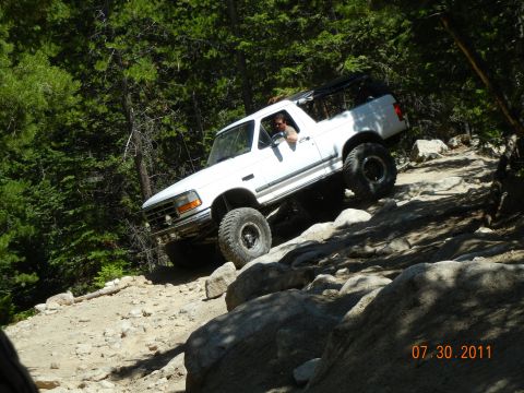 1996 Ford Bronco - A white 1996 Ford Bronco navigates a challenging rocky trail on a sunny day.