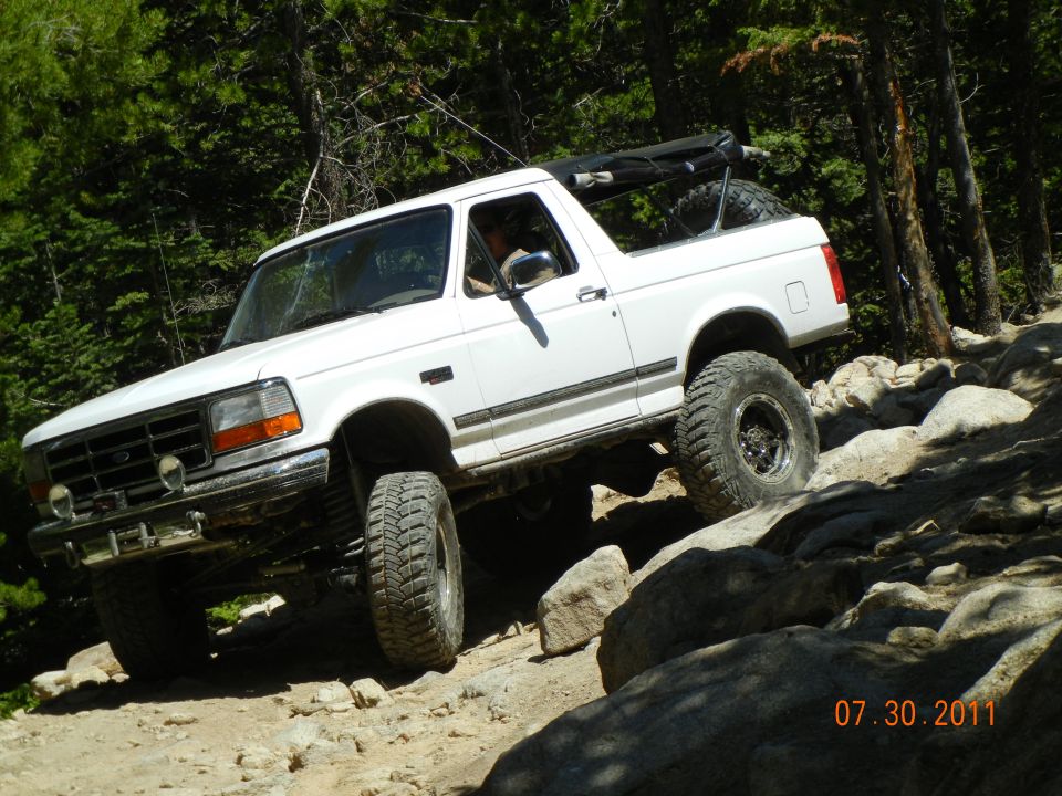 White 1996 Ford Bronco climbing over rocks on a dirt trail