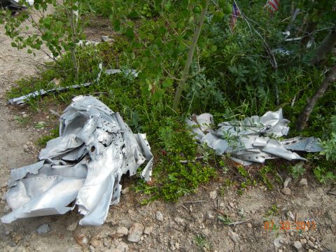 1996 Ford Bronco - Debris is scattered on the ground, partially covered by vegetation, with American flags visible in the distance.