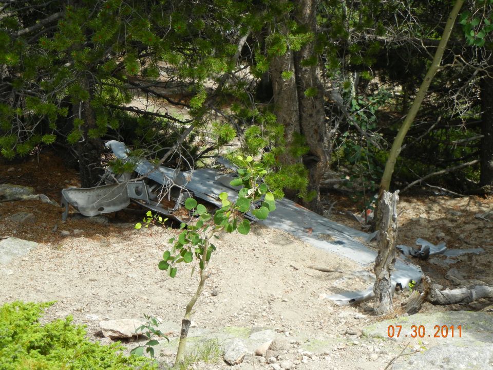 Aircraft wreckage lies on the ground among trees and rocks. A date stamp reads 07.30.2011