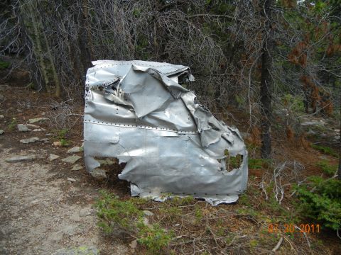 1996 Ford Bronco - Debris of a vehicle lies scattered in a wooded area, showing significant damage.