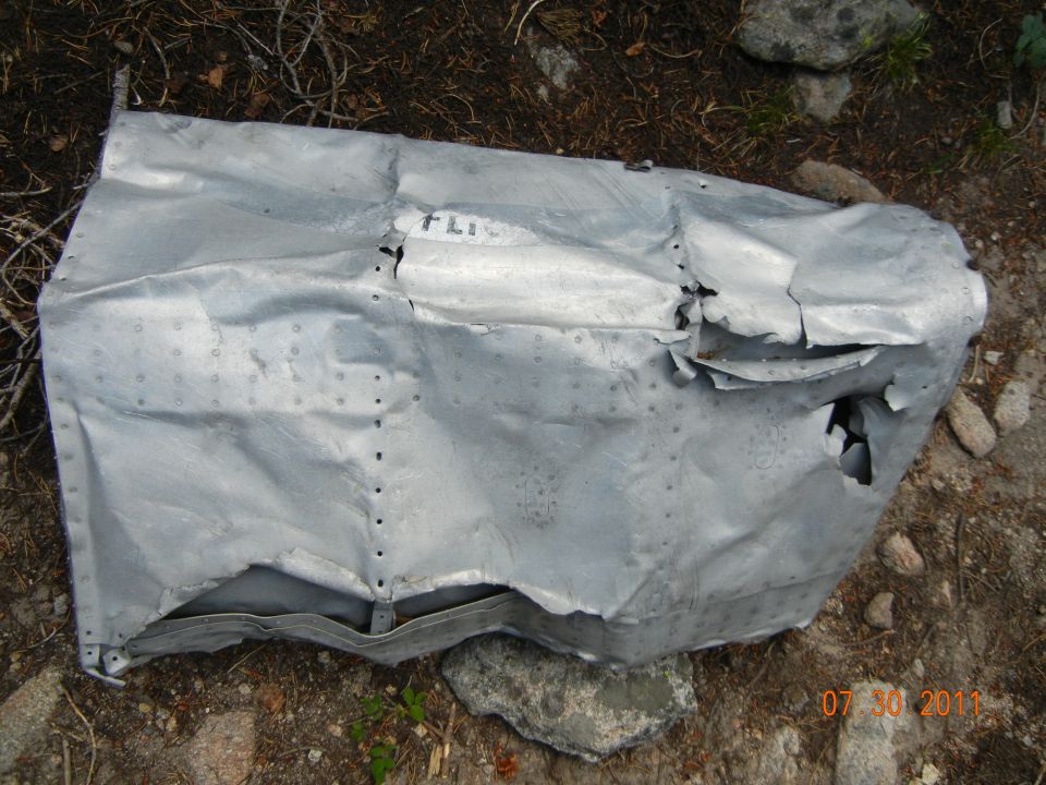 Damaged aluminum fuselage section with 'FLI' visible, resting on the ground