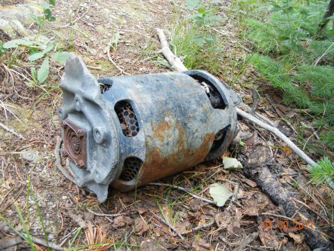 1996 Ford Bronco - A rusted motor part rests on the forest floor, surrounded by leaves and pine needles.