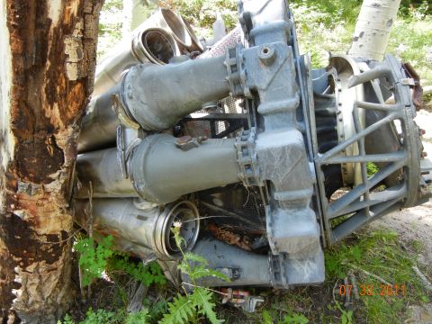1996 Ford Bronco - A large, complex metal component, possibly from an aircraft or industrial machinery, rests outdoors near trees.