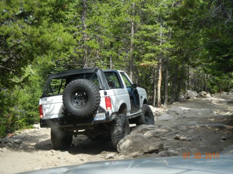 1996 Ford Bronco - A white 1996 Ford Bronco navigates a challenging rocky trail surrounded by trees.