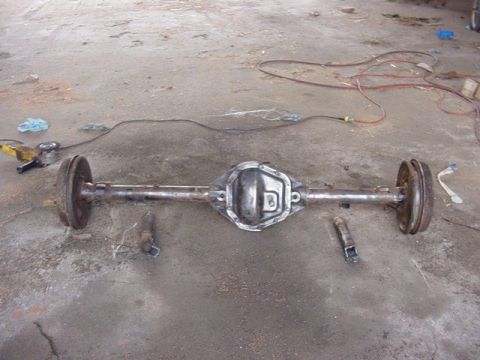 1992 Ford Bronco - A rear axle assembly sits on a concrete floor with tools and electrical cords scattered around.