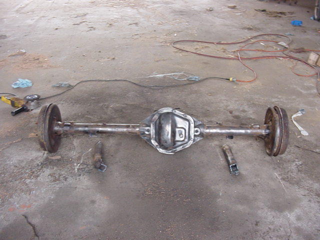 Rear axle assembly with drum brakes on a concrete floor, tools nearby