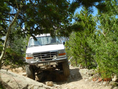 1996 Ford Bronco - White Ford Bronco tackling a challenging rocky trail surrounded by trees.