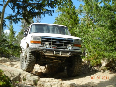 1996 Ford Bronco - A white Ford Bronco navigates a challenging rocky terrain on a sunny day.