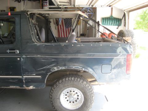 1995 Ford Bronco - Side view of a dark green 1995 Ford Bronco with its top removed and visible body damage.