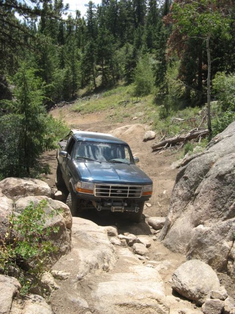 1995 Ford Bronco - This blue 1995 Ford Bronco tackles a challenging off-road path, demonstrating its capability on terrain.