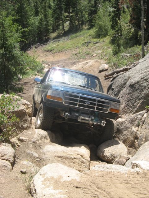 1995 Ford Bronco - 1995 Ford Bronco tackling a challenging off-road path with large rocks.