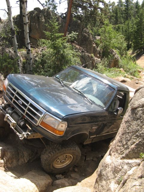 1995 Ford Bronco - A dark green Ford Bronco navigates a rocky trail, demonstrating its off-road capabilities.