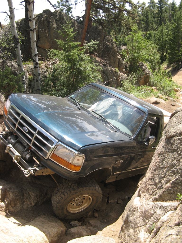 Dark green 1992 Ford Bronco off-roading over rocks, front winch visible