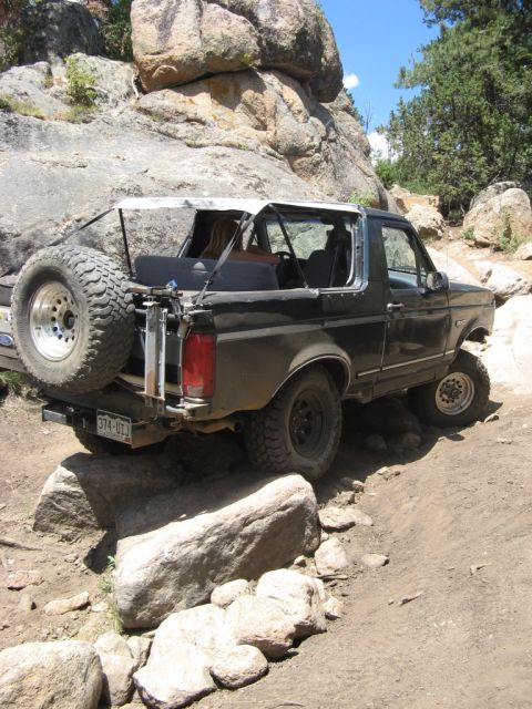 1995 Ford Bronco - A black Ford Bronco navigates a challenging rocky terrain on a sunny day.