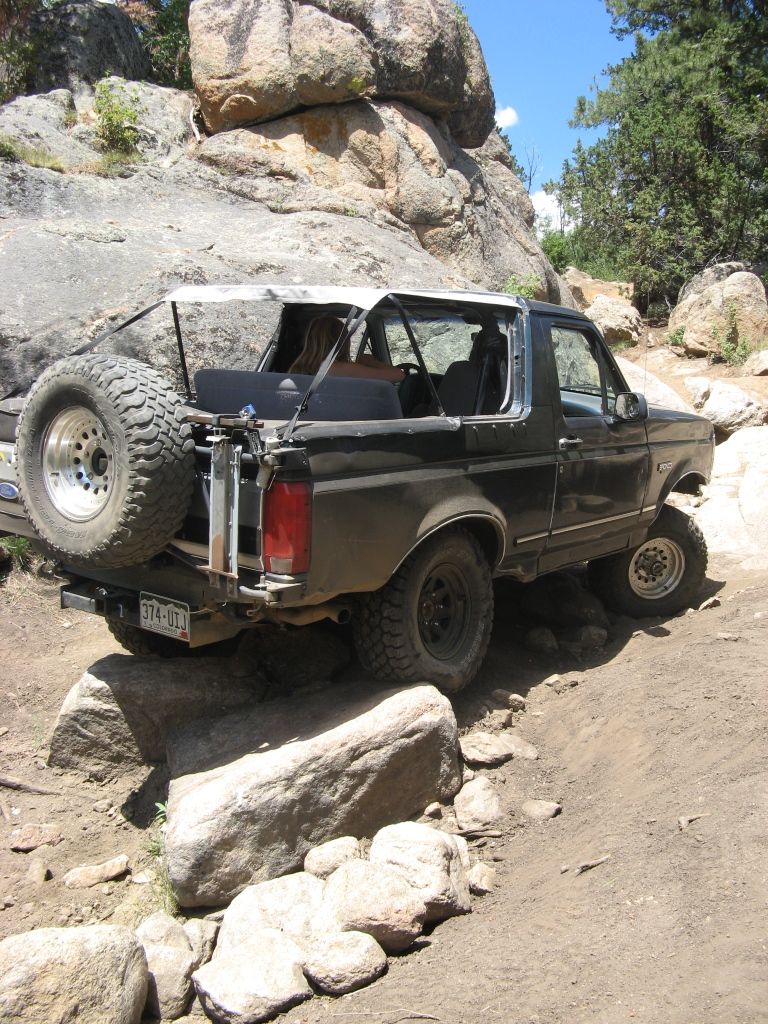 Black Ford Bronco with a spare tire on the back, driving on a rocky trail