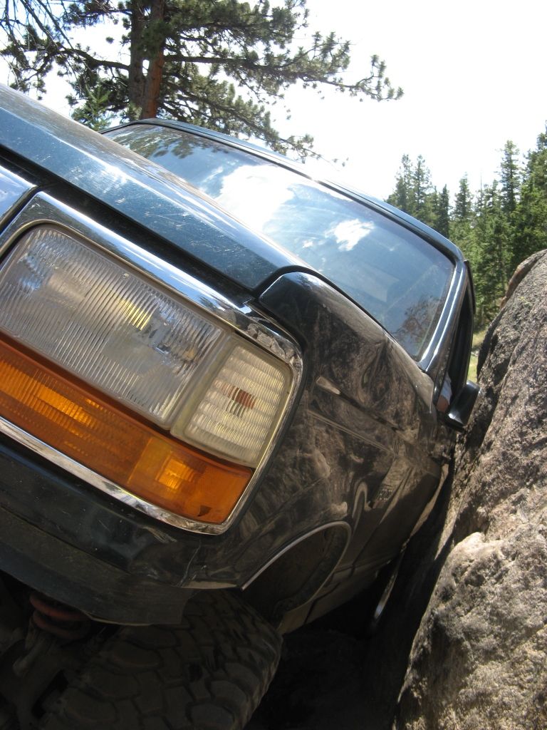Dark green SUV wedged between rocks, showing front fender, headlight, and windshield