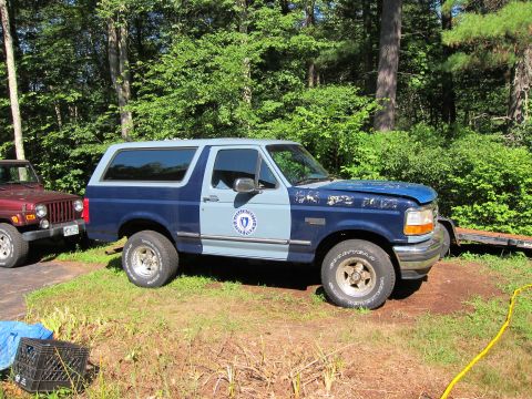 1991 Ford Crown Victoria LTD - A two-tone blue and light blue Ford Bronco is parked next to a red Jeep.