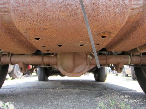 1991 Ford LTD Crown Victoria - The heavily rusted undercarriage of a vehicle, showing the rear axle and exhaust pipes, with other vehicles in the background.
