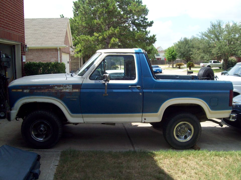 Blue and tan Ford Bronco SUV with white top parked in driveway, side view