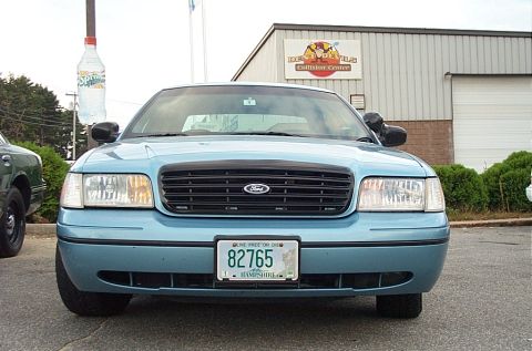 2001 Ford Crown Victoria - A light blue Ford Crown Victoria is parked in front of a collision center with a large Sprite bottle sign overhead.