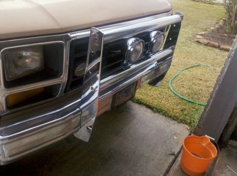 1988 Ford Bronco - Close-up of the front of a tan SUV, a chrome bull bar with two auxiliary lights and a prominent grille.
