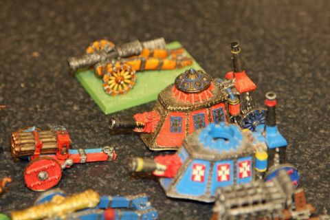 1978 Chevrolet C/K Pickup - A collection of miniature fantasy artillery pieces, including cannons and wheeled carriages, are arranged on a dark surface.