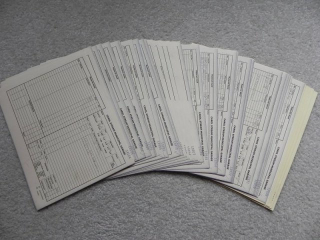 Fanned stack of printed vehicle paperwork on gray carpet