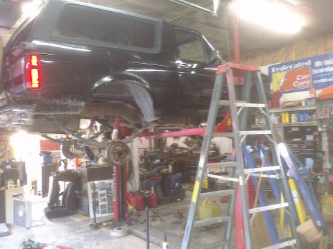1995 Ford Bronco - A black 1995 Ford Bronco is elevated on a car lift in a garage, undergoing service.