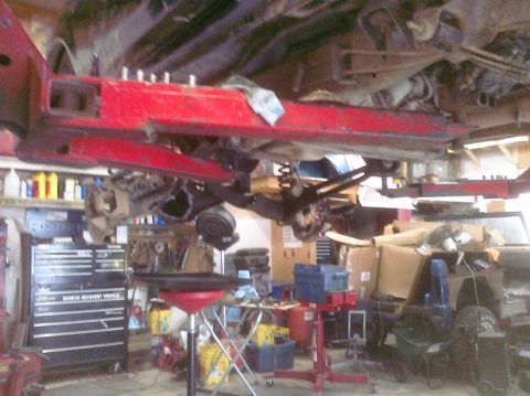1995 Ford Bronco - The underside of a vehicle is suspended on a lift, revealing its frame and suspension components in a workshop setting.