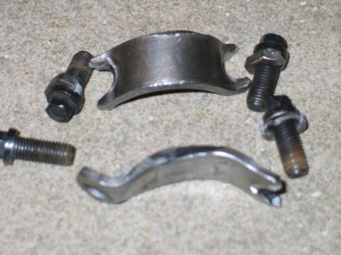 1984 Ford Bronco - Several metal automotive parts and bolts are scattered on a concrete surface.