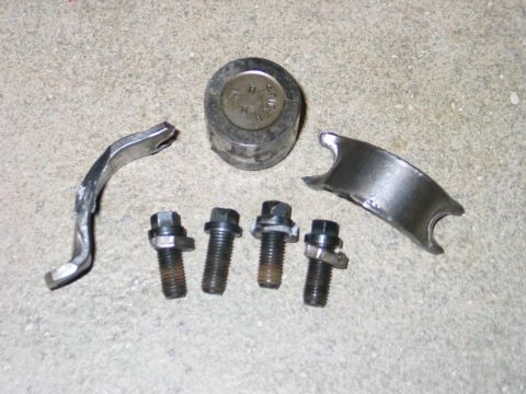 1984 Ford Bronco - Engine parts including a bearing cap, bolts, and a cylindrical component are laid out on a concrete surface.