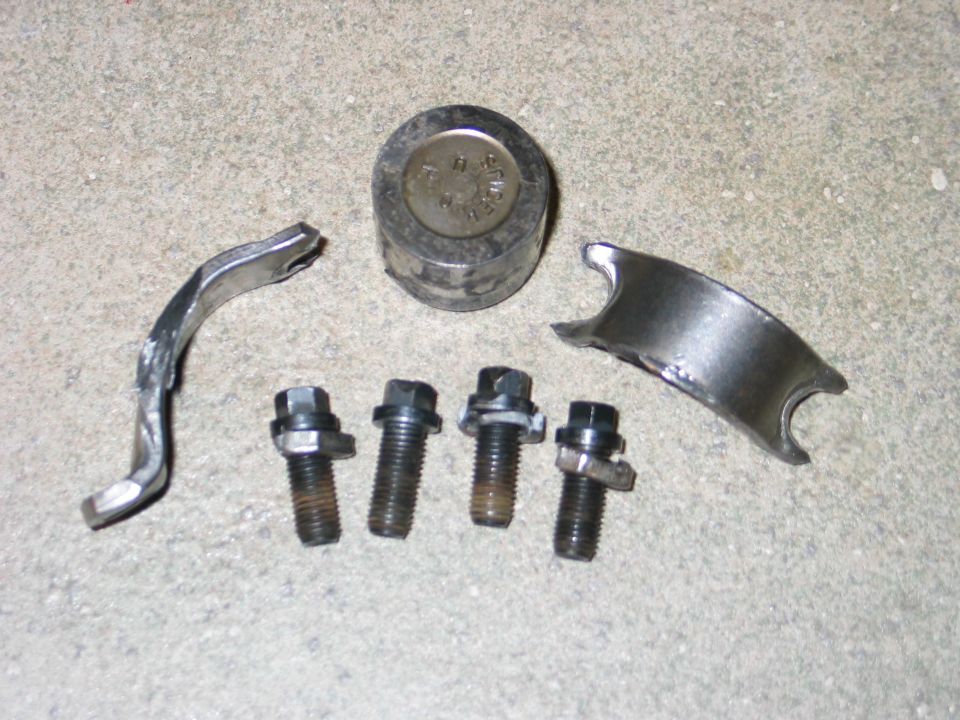 Engine bearing cap, four bolts, and a cylindrical component on a concrete surface