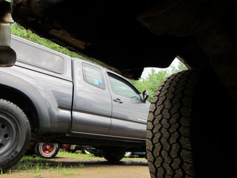 1991 Ford LTD Crown Victoria - Side view of a gray pickup truck parked under another vehicle, with a tire in the foreground.