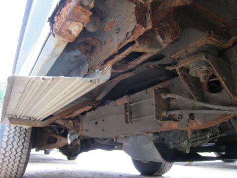 1991 Ford LTD Crown Victoria - The vehicle's undercarriage displays severe rust and structural degradation, indicating significant wear and tear.