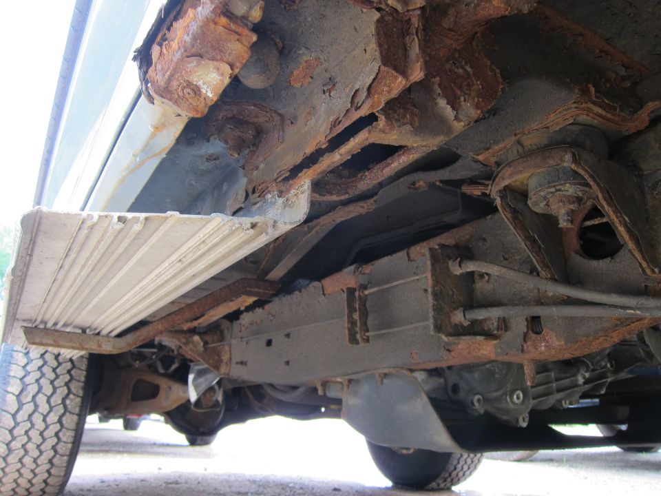 Undercarriage of a heavily rusted vehicle, showing extensive frame damage and corrosion