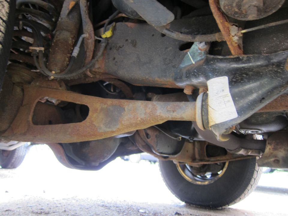Underside view of rusty suspension components and differential. White sticker with text is visible on a bracket
