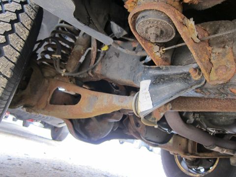 1991 Ford LTD Crown Victoria - The heavily rusted undercarriage of a vehicle is visible, with suspension and exhaust parts showing significant corrosion.