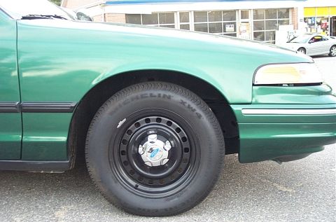 2001 Ford Crown Victoria - Front quarter view of a green 2001 Ford Crown Victoria, showing the fender and wheel. A silver car is in the background.