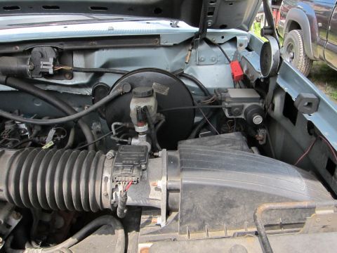1991 Ford LTD Crown Victoria - The engine bay of a vehicle, showing various components and a glimpse of another vehicle outside.