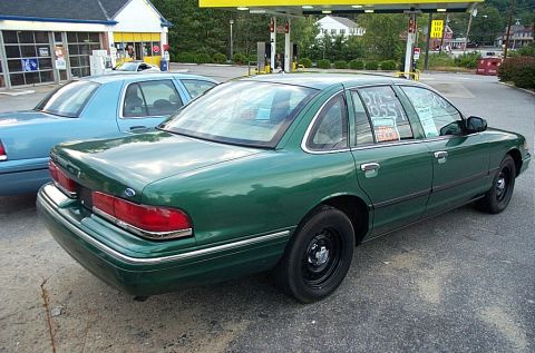 2001 Ford Crown Victoria - Two Ford Crown Victorias are parked at a gas station, one green and one blue, with sale signs visible in the windows.