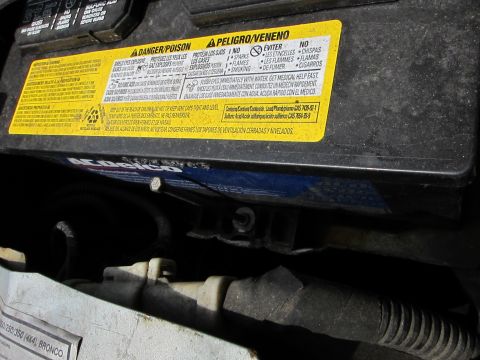 1991 Ford LTD Crown Victoria - A close-up view of a car battery, a prominent yellow warning label with safety instructions in multiple languages.