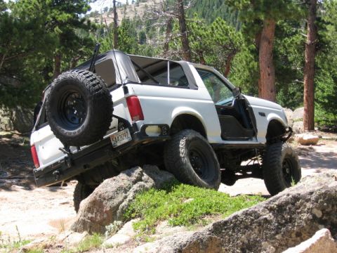 1995 Ford Bronco - White full-size Bronco-style SUV with the top and doors removed, flexing over a granite ledge on a pine-shaded mountain trail. It runs a li…