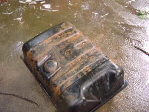 1986 Ford Bronco - A rusty gas tank rests on a wet, debris-covered surface.
