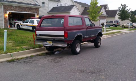 1993 Ford Bronco - A two-tone Ford Bronco is parked on the street in front of a residential garage.