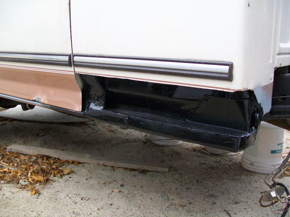White and tan truck rocker panel with black undercoating, showing rust repair and new paint